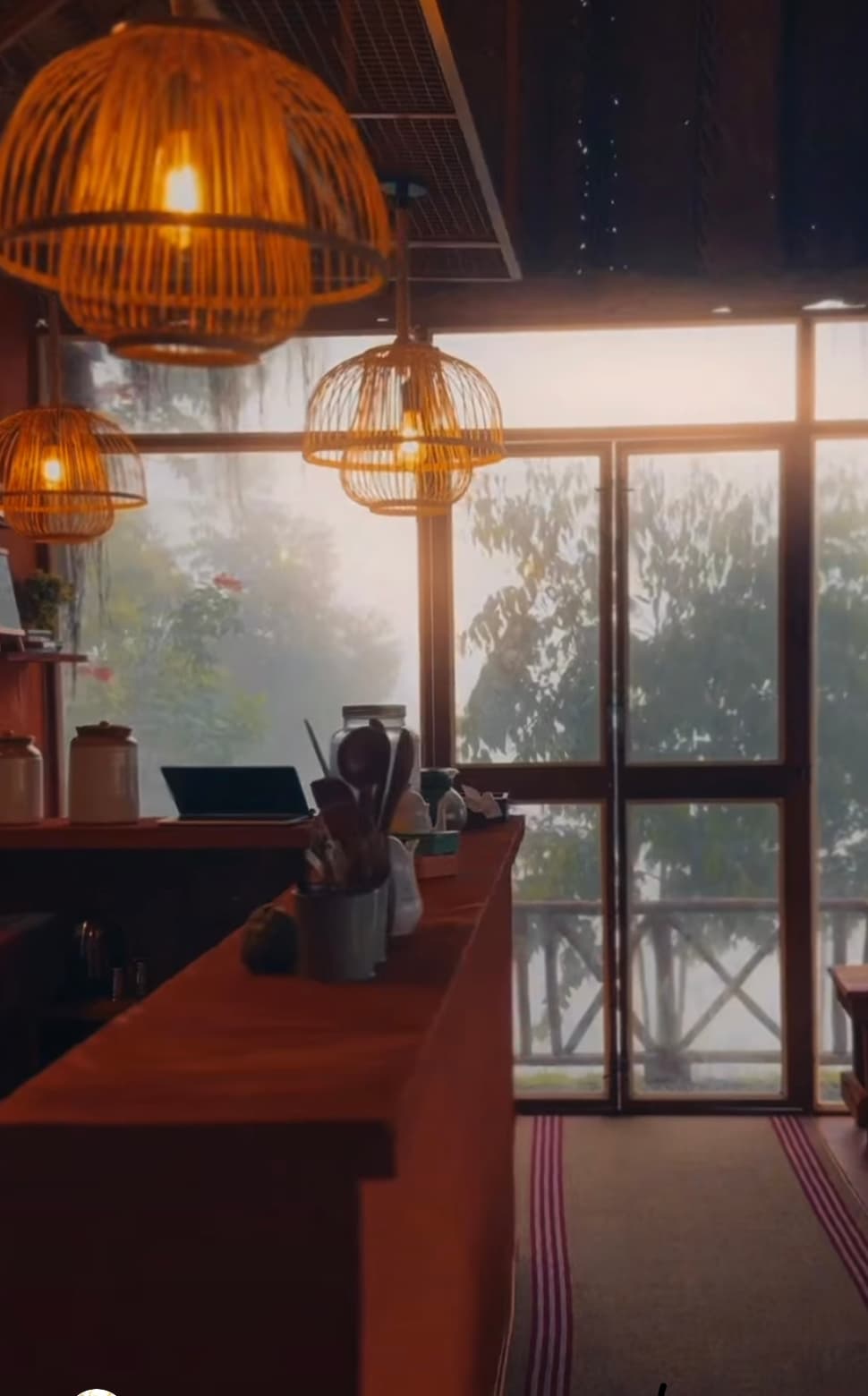 Woven pendant lamps above a wooden counter, with misty trees outside the window
