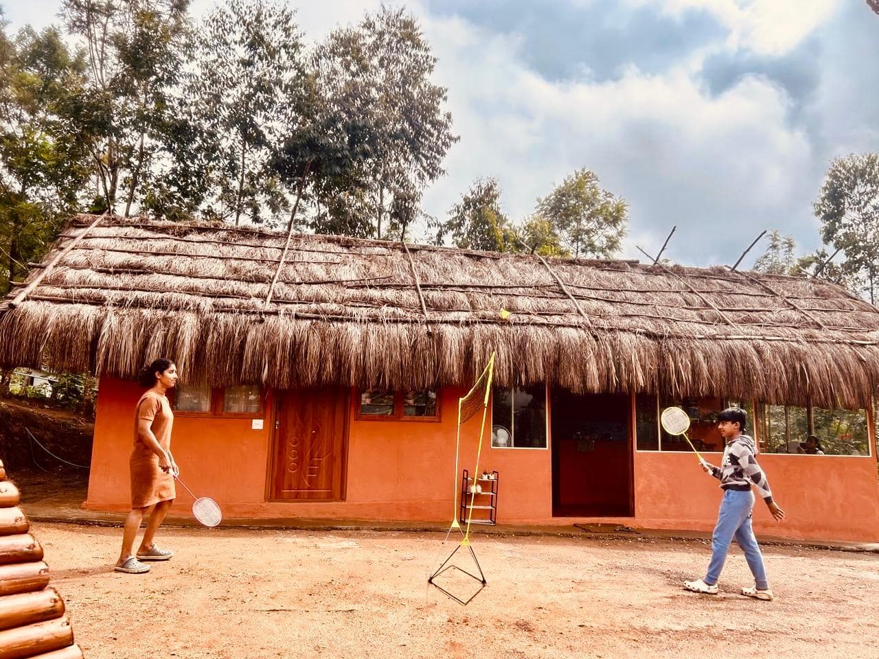 A thatched mud house with guests playing badminton outside