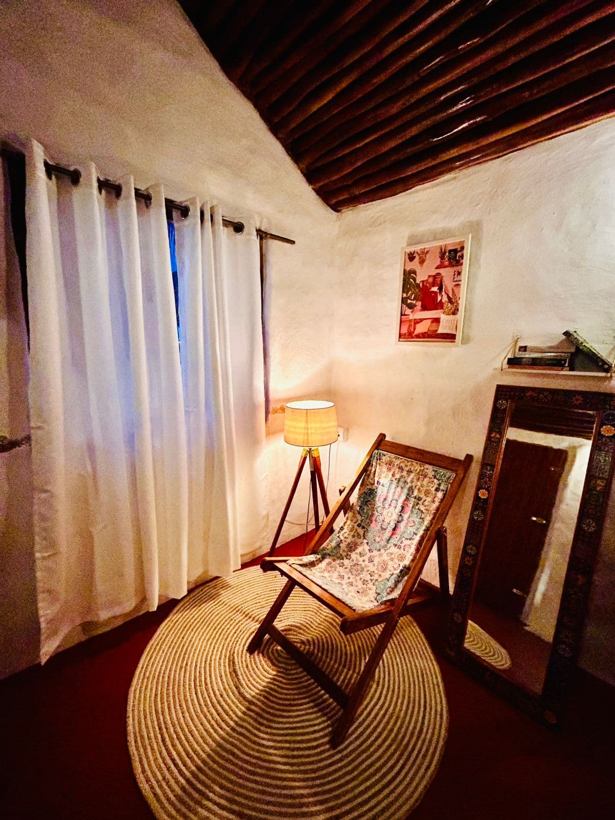A mud house interior with sheer curtains, a floor lamp and a folding chair